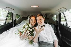 young happy bride and groom are rejoicing after the wedding ceremony in their car photo