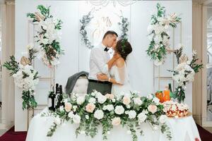 Presidium of the bride and groom at the wedding. Everything is ready for the wedding celebration. The groom and the bride are kissing on the background of a squat. Wedding banquet photo
