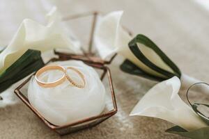 Tres calla lirio boutonnieres y oro Boda anillos en un vaso caja foto