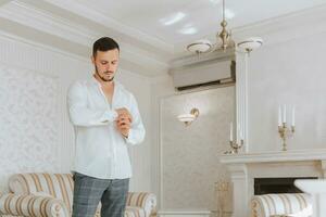 A stylish groom is getting dressed, preparing for the wedding ceremony. Groom's morning. Businessman wearing white shirt, male hands, groom getting ready in the morning before the wedding ceremony photo