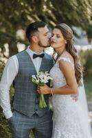 un joven Boda Pareja disfruta romántico momentos en el calle en contra el antecedentes de un verano bosque. el novia en un Boda vestido, el novio en un blanco camisa, chaleco y arco Corbata foto