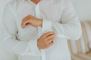 A stylish groom is preparing for the wedding ceremony. Groom's morning. Businessman wearing white shirt, male hands close-up, groom getting ready in the morning before the wedding ceremony photo