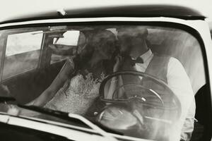 a luxurious and elegant wedding couple tenderly embrace in the middle of a stylish retro car. The photo was taken through the windshield. gorgeous bride and handsome groom in retro style.