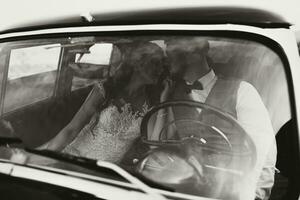 un lujoso y elegante Boda Pareja tiernamente abrazo en el medio de un elegante retro coche. el foto estaba tomado mediante el parabrisas. maravilloso novia y hermoso novio en retro estilo.