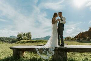 elegante novia y novio abrazo y Beso en contra el antecedentes de verano montañas. el concepto de un rústico Boda en el montañas, contento bohemio recién casados. foto