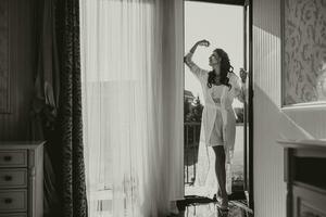 A beautiful bride in a white robe on the balcony of a hotel with a view of a big city. On your wedding day before marriage. photo