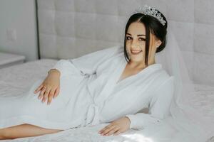 A beautiful bride girl in a white robe, veil and tiara on her head, the sun shines on her from the window. Happy young girl under the glare of sunlight. wedding concept photo