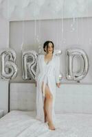 A beautiful bride girl in a white robe, veil and tiara on her head, the sun shines on her from the window. Happy young girl under the glare of sunlight. wedding concept photo