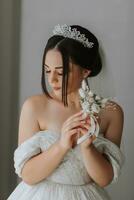 the groom's boutonniere is arranged from rose flowers in the hands of the bride with a French manicure in the wonderful natural light from the window photo