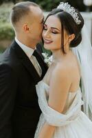 European wedding couple in the park. The bride in a beautiful dress with a long train and sleeves. Groom in a classic suit photo