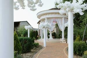el cerrado Boda arco en el parque es hecho de blanco flores en blanco columnas lejos Boda ceremonia. foto