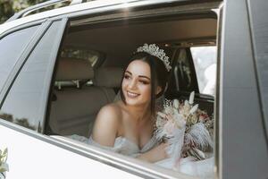 the bride sits in a white luxury car on the wedding day with a bouquet. Portrait of the bride. lush white lace dress. photo