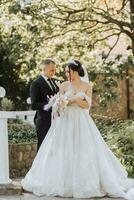 European wedding couple in the park. The bride in a beautiful dress with a long train and sleeves. Groom in a classic suit photo