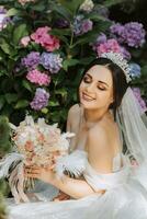 joven hermosa novia en Boda vestir con abierto espalda y corona en su cabeza sentado cerca hortensia flores, Moda foto tomado debajo duro luz de sol