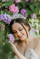 joven hermosa novia en Boda vestir con abierto espalda y corona en su cabeza sentado cerca hortensia flores, Moda foto tomado debajo duro luz de sol