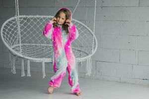 Portrait of happy little girl on porch sitting on wicker swing and playing in pink pajamas photo