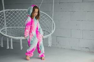 Portrait of happy little girl on porch sitting on wicker swing and playing in pink pajamas photo