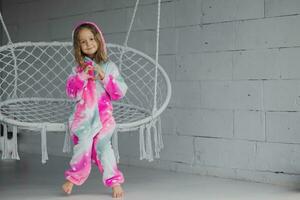 Happy little girl sitting on a wicker swing on the porch and playing in pink pajamas and making a heart shape with her hands. Children's friendship. photo