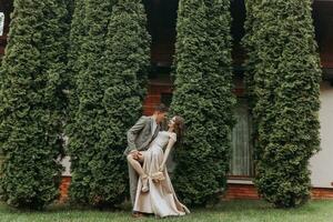 Groom and bride in the park in nature, green thuja trees on the background. Kiss. Photo portrait. Wedding couple