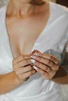 The bride is holding a luxurious gold ring with a diamond. Beautiful hands and manicure. Open neckline. Cropped photo