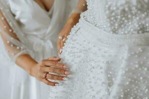 white wedding dress on a mannequin in the room, close-up of the bride's hand on the mannequin. Wedding details, modern wedding dress with long train, long sleeves and open back photo