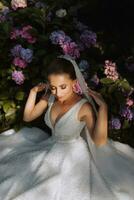 young beautiful bride in off-shoulder wedding dress near hydrangea flowers, fashion photo taken under soft sunlight