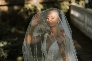 Wedding portrait of the bride. Beautiful blonde bride in a white dress under a long veil in the forest. photo