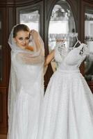 Stylish bride with wedding hairstyle and makeup in white robe standing near her wedding dress. photo