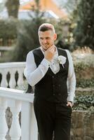 candid portrait of young stylish groom in classic black suit with waistcoat, white shirt photo