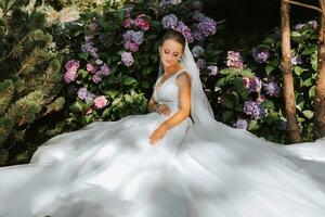 young beautiful bride in off-shoulder wedding dress near hydrangea flowers, fashion photo taken under soft sunlight