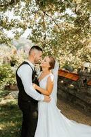 The bride and groom are standing and embracing in a beautiful yard. Wide angle photo of the sunset.