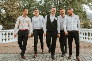 Cheerful, young, energetic groom's witnesses in white shirts next to the groom. Friends congratulate the groom. photo