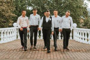 Cheerful, young, energetic groom's witnesses in white shirts next to the groom. Friends congratulate the groom. photo