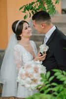 portrait of groom and brunette bride in dress with sleeves in green leaf on veranda photo