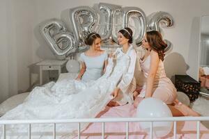 A beautiful young bride and her girlfriends are standing on the bed and celebrating a bachelorette party. Final preparations for the wedding. The bride is waiting for the groom. Morning, bride. photo