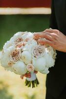 Photo of the groom in a classic black suit and glasses, with a bouquet of flowers in his hands