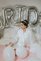 A beautiful brunette bride in a white robe, a veil and a tiara on her head, sits on a bed. Inscription bride. Happy young girl under the glow of sunlight. wedding concept photo