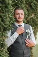 handsome groom in an elegant suit. A bearded young man in a stylish tie, a white shirt and a fashionable gray vest. Fashionable portrait. photo