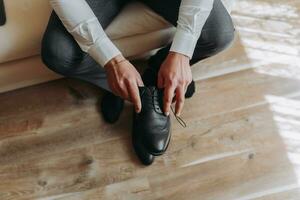 Man in suit, groom, close-up putting on shoes, holding black shoes, tying shoelaces photo