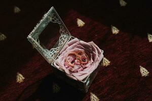 Photo of wedding accessories. Luxurious bouquet of the groom. Gold rings on a stand with flowers, a black classic watch on a burgundy background.