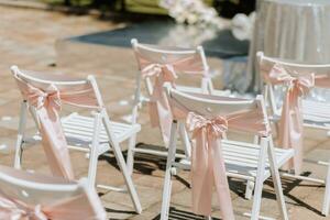 Boda ceremonia en el patio trasero. redondo arco hecho de flores y muchos blanco sillas con rosado cintas Boda tema. fiesta concepto foto