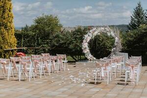 Wedding ceremony in the yard. Round arch made of flowers and many white chairs with pink ribbons. Wedding theme. Holiday concept photo