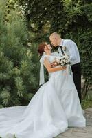 portrait of the bride and groom in the park, the bride and groom are hugging and tenderly kissing. Wedding walk in the park. Long train of the dress photo