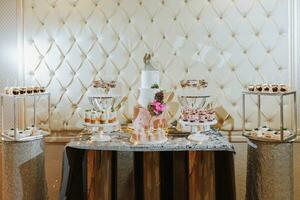 A delicious wedding. White cake decorated with flowers. Candy bar for a banquet. Celebration concept. Fashionable desserts. Table with sweets, candies. Fruits photo