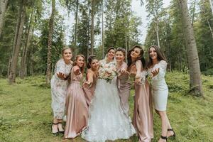 A group of beautiful girls with a bride in identical dresses are smiling, celebrating and having fun together against the background of nature and tall trees. Girls party photo