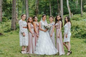 A group of beautiful girls with a bride in identical dresses are smiling, celebrating and having fun together against the background of nature and tall trees. Girls party photo