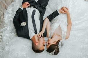 a young beautiful bride with blue eyes in a wedding dress, lying on stone steps, her husband is next to her. The photo is taken from above