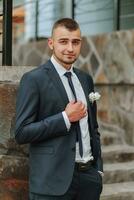 un hombre en un clásico traje y blanco camisa poses cerca un Roca pared. de los hombres estilo. moda. negocio. foto