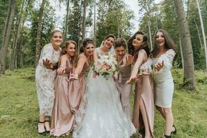 A group of beautiful girls with a bride in identical dresses are smiling, celebrating and having fun together against the background of nature and tall trees. Girls party photo