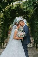 un Boda Pareja es disfrutando el mejor día de su vida en contra el antecedentes de verde hojas en el parque. retrato de novias en amor en naturaleza foto